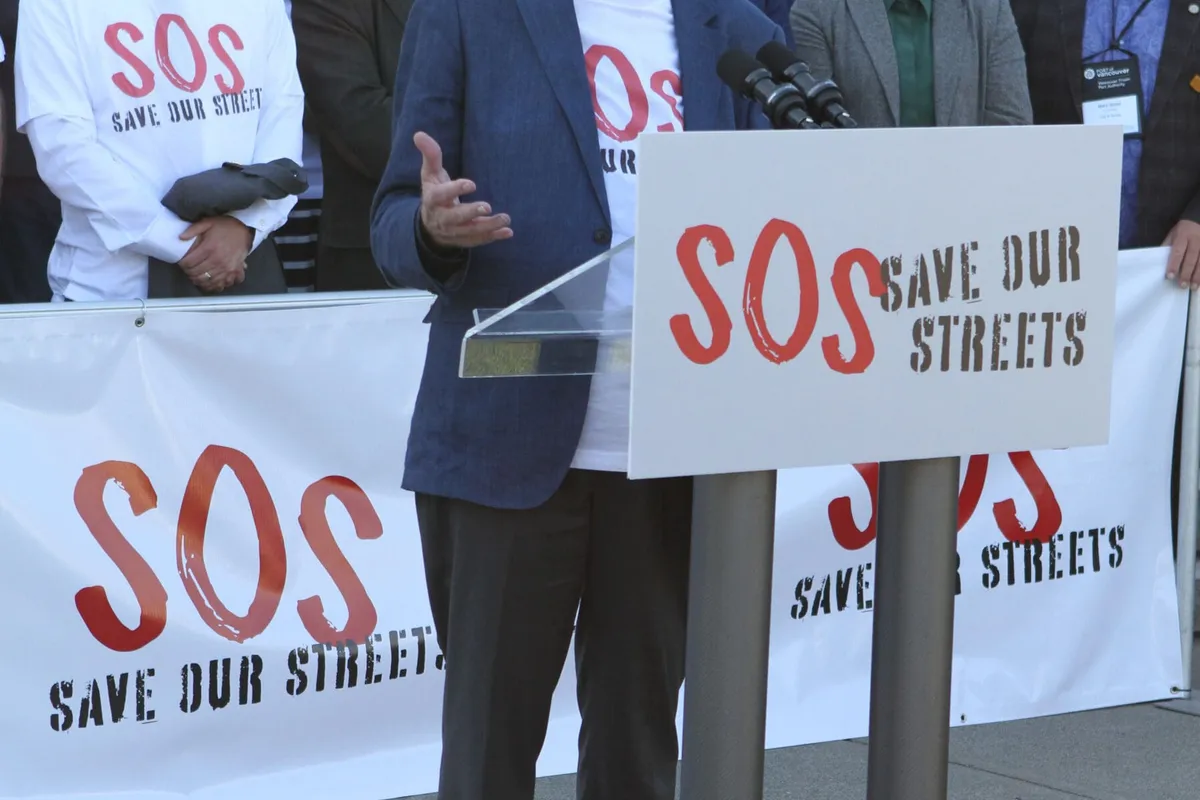 A speaker at a Save Our Streets podium, in front of the coalition’s banner, at the Mayors Rally on the steps of the BC Legislature