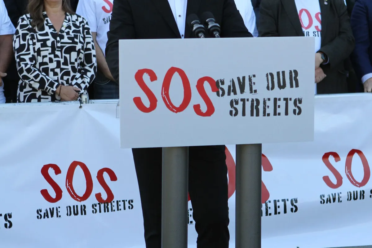 A Save Our Streets podium sign in front of the rally banner