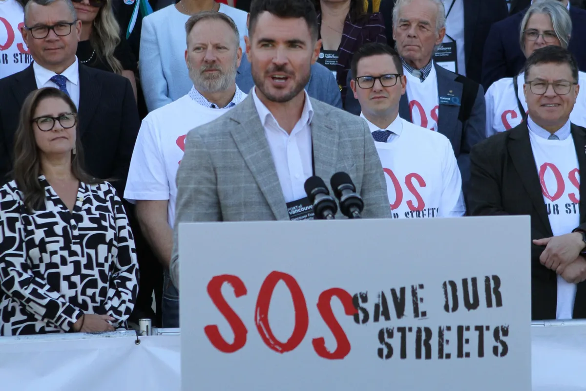 A speaker at the rally microphones, with people in Save Our Streets T-shirts behind