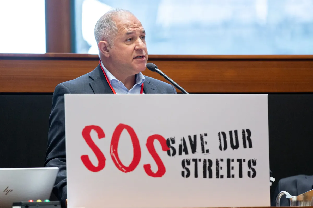 A speaker at the Forum behind a Save Our Streets podium sign